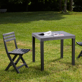 Conjunto de cadeira dobrável e mesa desmontável IPAE PROGARDEN em plástico cinzento, com assento e encosto com ranhuras, exibida em vista frontal ligeiramente inclinada para a direita.